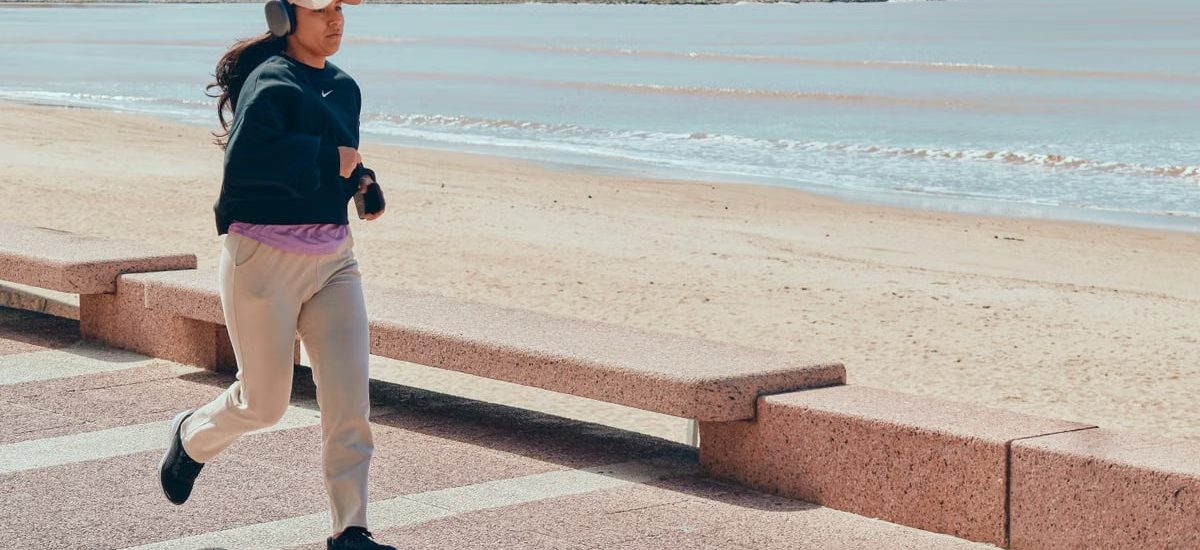 A woman jogs along the beachfront pathway in Montevideo, Uruguay, enjoying a sunny day.