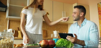 🎬 FULL 4K VIDEO for this still is in my bio link! ⬇️ Attractive couple chatting in the kitchen early morning. Beautiful woman feed her husband while cooking breakfast at home