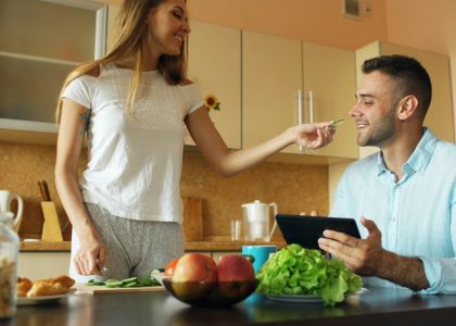 🎬 FULL 4K VIDEO for this still is in my bio link! ⬇️ Attractive couple chatting in the kitchen early morning. Beautiful woman feed her husband while cooking breakfast at home