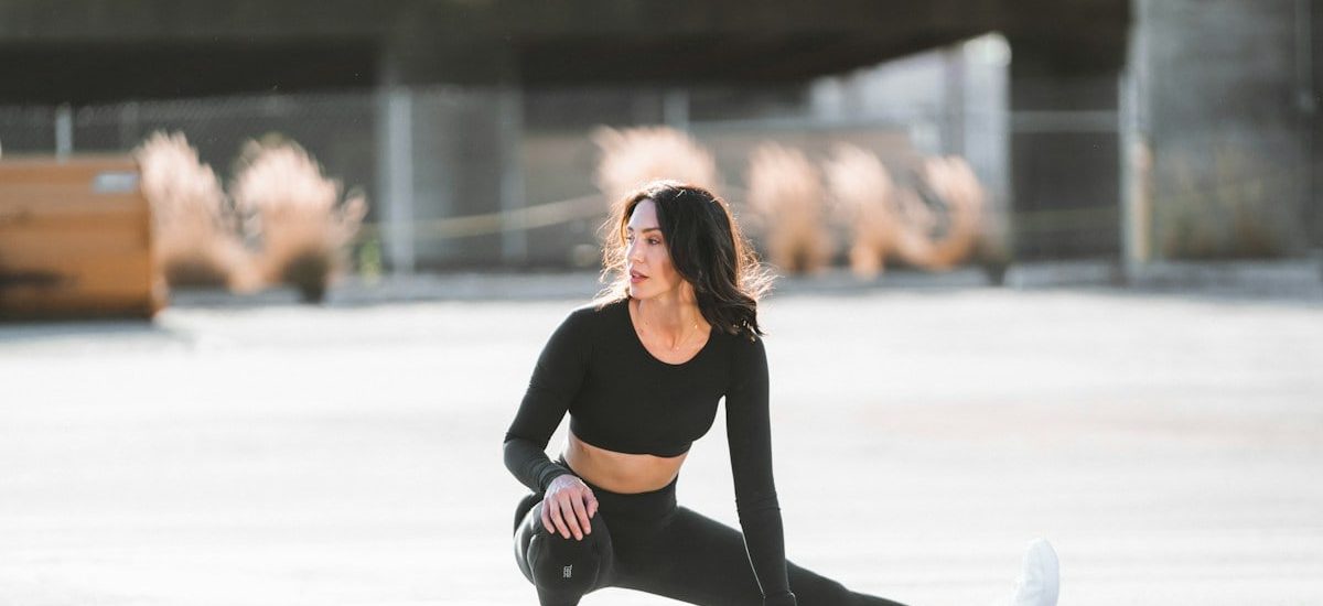 woman in black tank top and black leggings holding black and white nike shoes